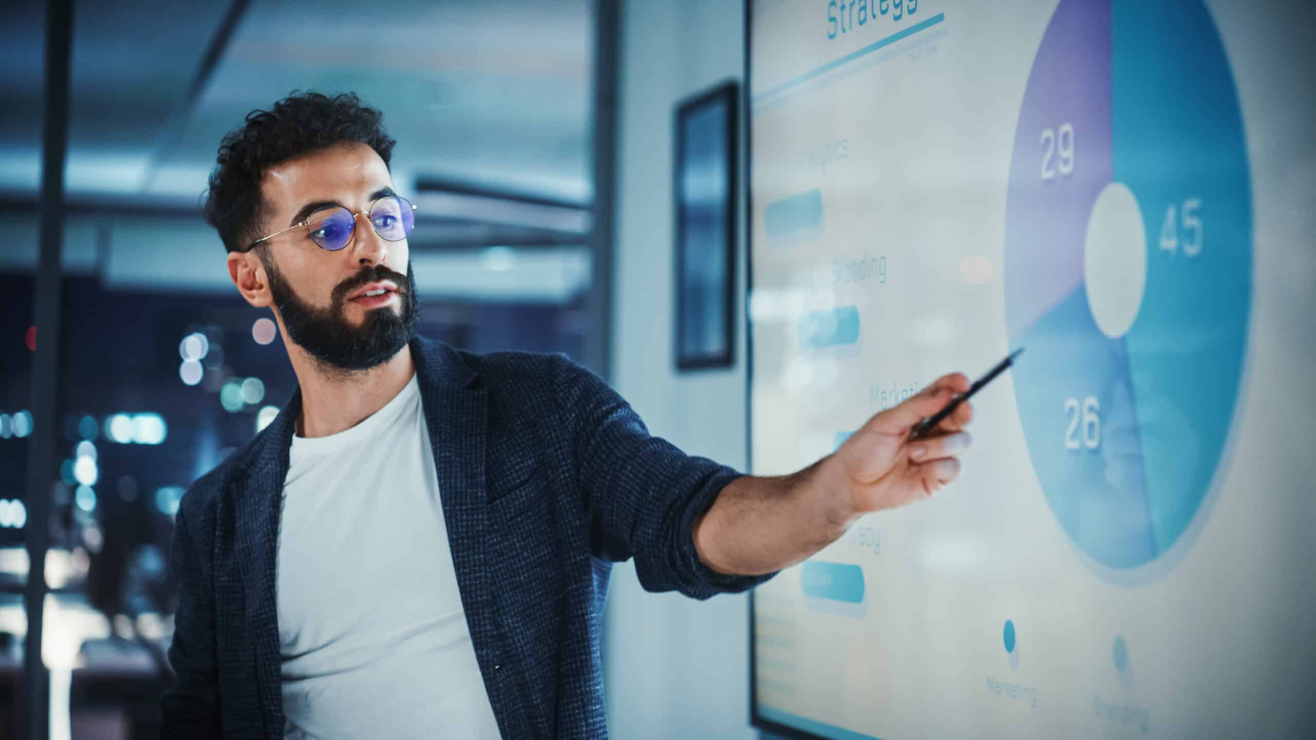 Company Creative Manager Holds Sales Meeting Presentation for Employees and Executives. Hispanic Male Uses TV Screen with Growth Analysis; Charts; Ad Revenue. Work in Business Office.